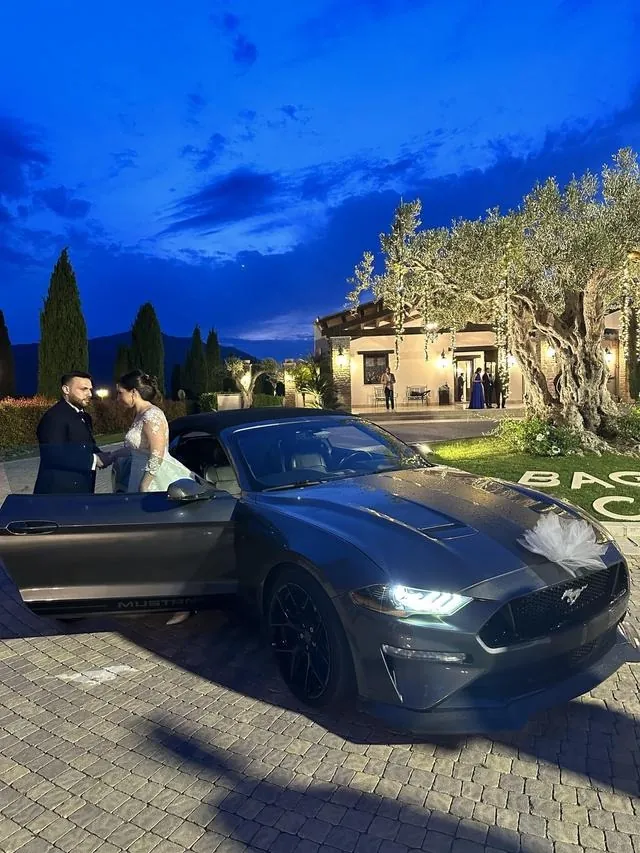 Sposi accanto alla Ford Mustang di sera, con le luci dei lampioni