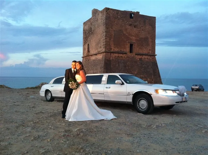 Sposi con la limousine accanto a una torre sul mare